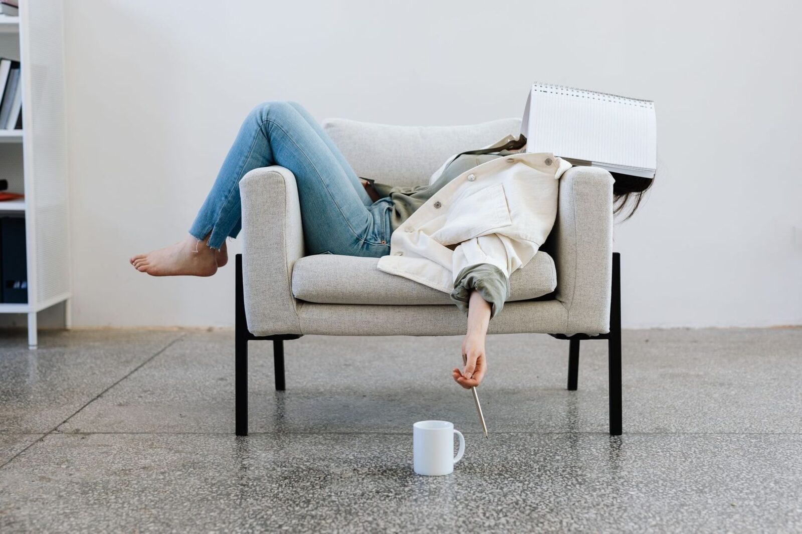 Person reclines in an armchair with a notebook covering their face