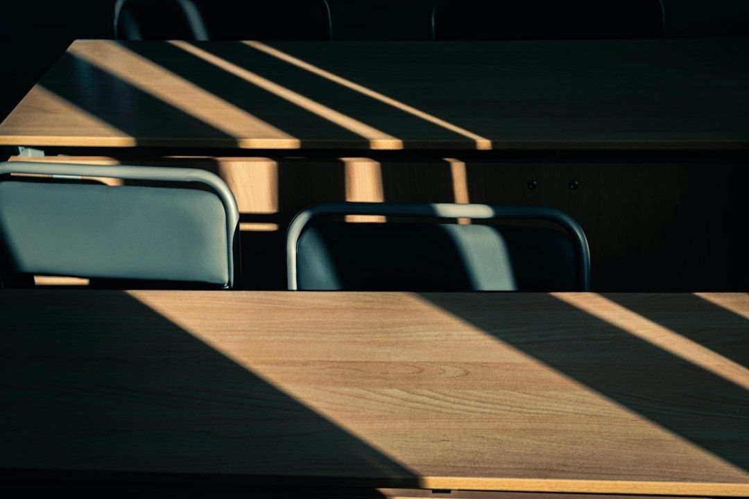 Quiet wooden desks and empty chairs crossed by soft window light